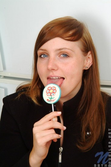Red haired teen babe Beth Nubiles slowly strips while eating a lollipop.