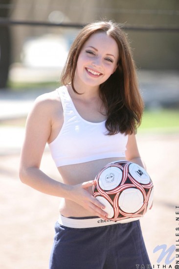 Smiling sportive girl Tabitha Nubiles in snow white top and blue shorts poses with a ball outside